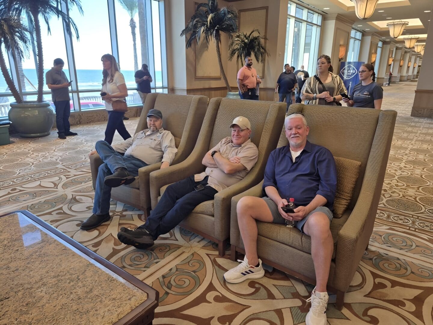 Three men sitting in hotel lobby chairs.