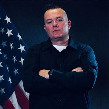 Man with folded arms beside American flag